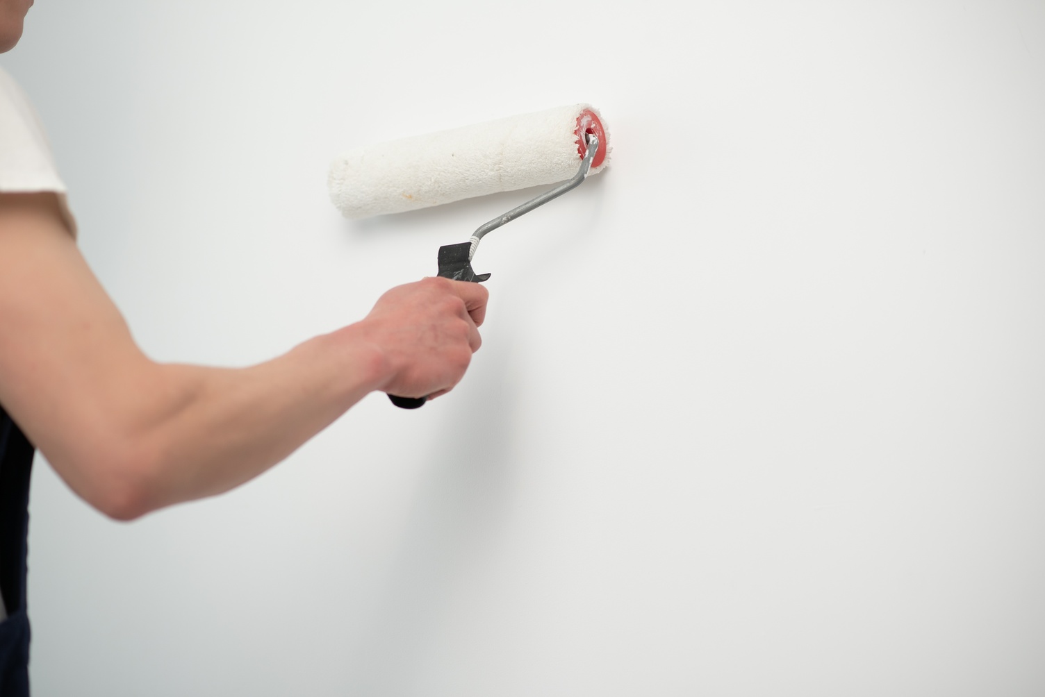 The painter is painting a wall in a room with a roller.